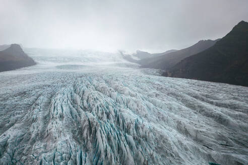 Weitläufiger Blick auf einen Gletscher mit zerklüfteten Gipfeln im Vatnajokull-Nationalpark unter einem dramatisch bewölkten Himmel. - ADSF50670