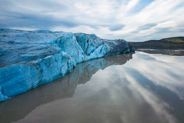 A captivating view of a glacier mirrored in the tranquil waters of Vatnajokull National Park, under a soft-lit sky. - ADSF50676