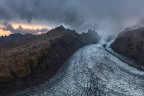 Ein atemberaubender Blick auf den Vatnajokull-Gletscher und die zerklüfteten Berge in der Abenddämmerung unter einem dramatischen isländischen Himmel. - ADSF50686