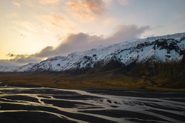 Der Sonnenuntergang wirft ein warmes Licht auf die schneebedeckten Berge neben den gemusterten Flussbetten des Thorsmork-Tals im isländischen Hochland - ADSF50696