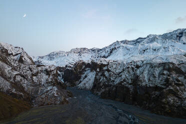 Dämmerung über der zerklüfteten Landschaft des Thorsmork-Tals mit einer Mondsichel über den schneebedeckten Bergen im isländischen Hochland - ADSF50697