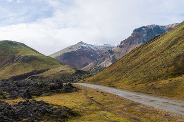 Eine heitere Aussicht auf das isländische Hochland mit grünen Tälern, Bergen und einer kurvenreichen Straße - ADSF50706