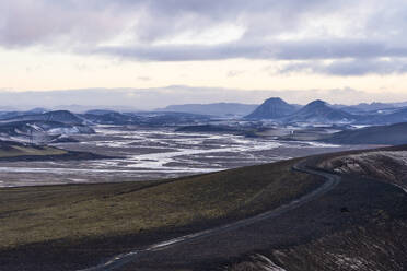 Ein ruhiger Blick auf kurvenreiche Straßen durch die abgelegene, trostlose Landschaft des isländischen Hochlands, mit gedämpften Farben und weitem Himmel - ADSF50710