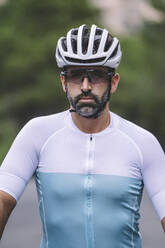 Porträt eines ernsthaften Radfahrers mit Helm und Sonnenbrille in einem blau-weißen Trikot - ADSF50723