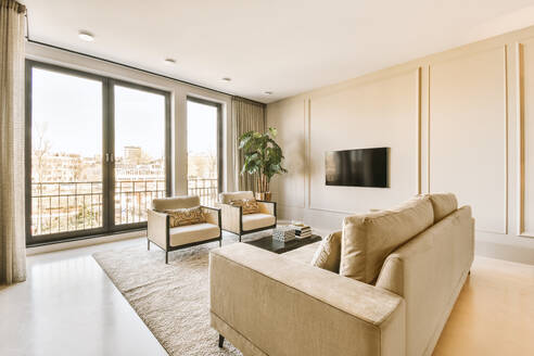 Couch und Sessel mit Couchtisch vor dem Fernseher vor dem hellen Fenster im weißen Wohnzimmer in einem modernen Haus - ADSF50734