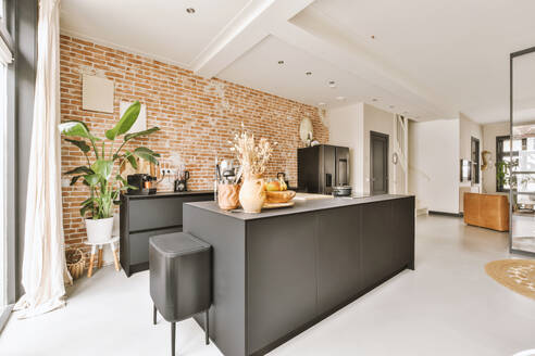 Früchte mit Dekor und Utensilien auf schwarzer Insel in moderner Küche gegen Backsteinwand in geräumiger Wohnung - ADSF50738