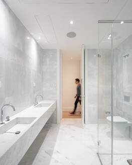 Duschkabine mit zwei Marmorwaschbecken und Toilettenbecken in einem beleuchteten, geräumigen Badezimmer mit weiß gefliesten Wänden in einem modernen Penthouse - ADSF50767