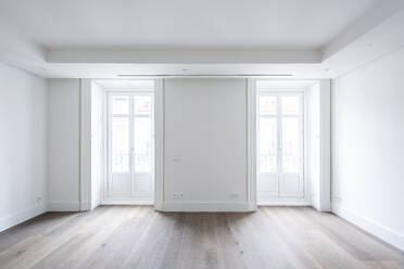 Weiße geschlossene Türen mit hellen Fenstern in einem geräumigen leeren Wohnzimmer eines modernen Penthouses mit hellen Wänden und Hartholzboden - ADSF50769