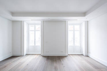 White closed doors of bright windows in spacious empty living room of contemporary penthouse with lights walls and hardwood floor - ADSF50769