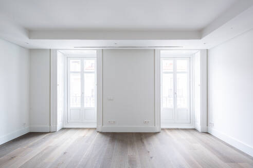 White closed doors of bright windows in spacious empty living room of contemporary penthouse with lights walls and hardwood floor - ADSF50769