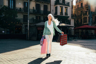 Beautiful senior woman with silver gray hair shopping outdoors in the city - Attractive cheerful mature female having fun, shopping and bonding, concepts about elderly lifestyle - DMDF07802