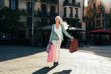 Schöne ältere Frau mit silbergrauen Haaren beim Einkaufen im Freien in der Stadt - Attraktive fröhliche reife Frau, die Spaß hat, einkauft und Kontakte knüpft, Konzepte für den Lebensstil älterer Menschen - DMDF07802