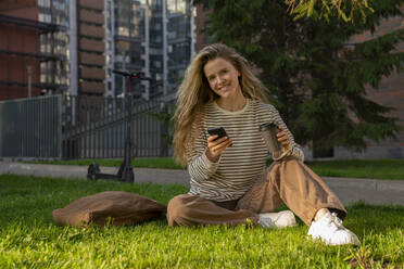 Lächelnde Frau mit Smartphone und Einwegbecher im Park - VPIF09104