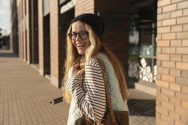 Lächelnde Frau mit Umhängetasche auf dem Fußweg stehend - VPIF09117