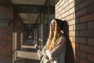Woman enjoying sunlight on face in front of brick wall - VPIF09125