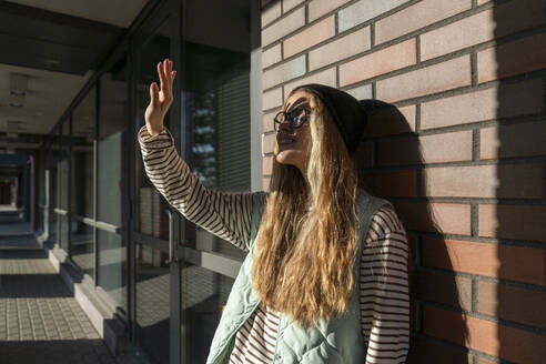 Blonde Frau, die ihre Augen vor einer Backsteinmauer vor dem Sonnenlicht schützt - VPIF09126