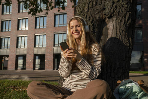 Smiling woman with smart phone listening to music through headphones - VPIF09140