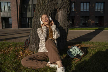 Frau genießt das Musikhören über kabellose Kopfhörer im Park - VPIF09142