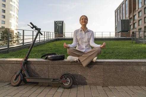 Geschäftsfrau meditiert Yoga sitzend an der Wand - VPIF09164