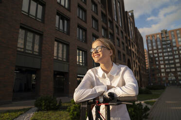 Smiling businesswoman with electric push scooter by building - VPIF09176