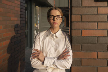 Confident businesswoman with arms crossed leaning on brick wall - VPIF09192