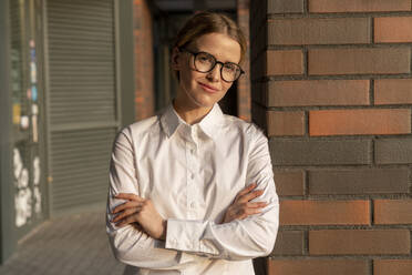 Businesswoman with arms crossed leaning on brick wall - VPIF09193
