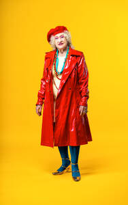 Schöne ältere alte Frau in schicken Partykleidern, die auf einem farbigen Hintergrund im Studio agiert - Konzeptbild über drittes Alter und Seniorität, alte Menschen, die sich innerlich jung fühlen. - DMDF07834