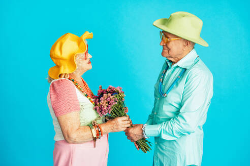 Schönes älteres altes Paar in schicker Partykleidung, das im Studio auf einem farbigen Hintergrund agiert. Konzeptbild über das dritte Lebensalter und das Alter, alte Menschen, die sich innerlich jung fühlen. - DMDF07867