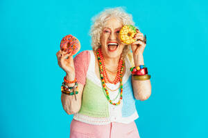 Schöne ältere alte Frau in schicken Partykleidern, die auf einem farbigen Hintergrund im Studio agiert - Konzeptbild über drittes Alter und Seniorität, alte Menschen, die sich innerlich jung fühlen. - DMDF07871