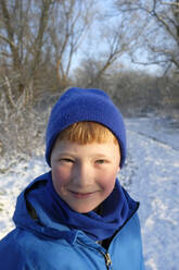 Smiling boy wearing knit hat in winter forest - GISF01013
