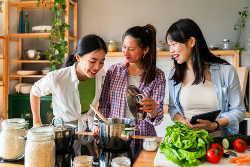 Happy beautiful chinese women friends bonding at home and cooking delicious meal together- Playful pretty asian female adults meeting and having fun at home, concepts about lifestyle, domestic life and friendship - DMDF07967