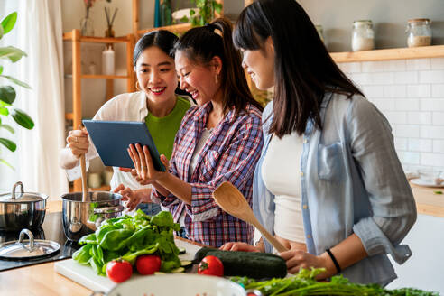 Happy beautiful chinese women friends bonding at home and cooking delicious meal together- Playful pretty asian female adults meeting and having fun at home, concepts about lifestyle, domestic life and friendship - DMDF07972