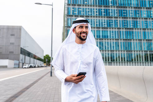 Arabischer Mann aus dem Mittleren Osten in traditioneller emiratischer Kandora-Kleidung in der Stadt - Arabischer muslimischer Geschäftsmann bei einem Spaziergang im städtischen Geschäftszentrum. - DMDF08055