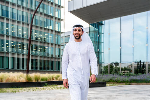 Arabischer Mann aus dem Mittleren Osten in traditioneller emiratischer Kandora-Kleidung in der Stadt - Arabischer muslimischer Geschäftsmann bei einem Spaziergang im städtischen Geschäftszentrum. - DMDF08069