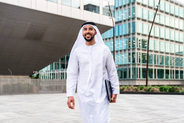 Arabischer Mann aus dem Mittleren Osten in traditioneller emiratischer Kandora-Kleidung in der Stadt - Arabischer muslimischer Geschäftsmann bei einem Spaziergang im städtischen Geschäftszentrum. - DMDF08072