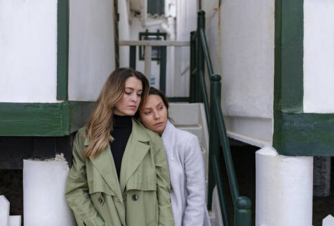 Woman leaning on girlfriend's shoulder in front of beach house - MMPF01114