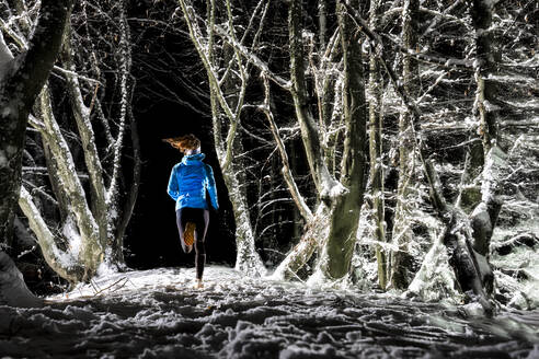 Woman running in winter forest at night - STSF03805