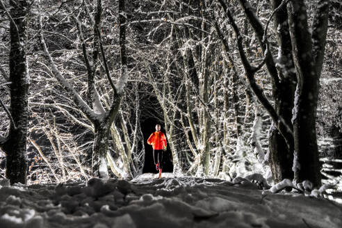 Man running on snow under trees in winter forest at night - STSF03807