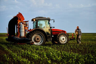 Landwirt, der in der Nähe eines Traktors im Maisfeld spazieren geht und die Pflanzen untersucht - NOF00850