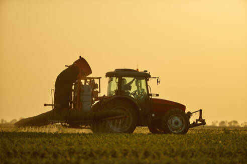 Älterer Landwirt im Traktor beim Sprühen von Dünger auf einem Maisfeld unter dem Himmel - NOF00853