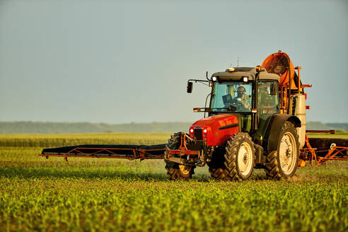 Landwirt im Traktor düngt Maisfeld bei Sonnenuntergang unter Himmel - NOF00856