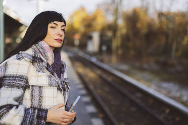 Schöne Frau mit Mobiltelefon, die am Bahnhof auf einen Zug wartet - JCCMF10997