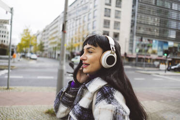 Frau hört Musik über drahtlose Kopfhörer auf einem Fußweg in der Stadt - JCCMF11009