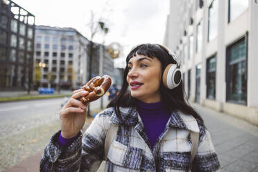 Woman having pretzel and listening to music through wireless headphones - JCCMF11010