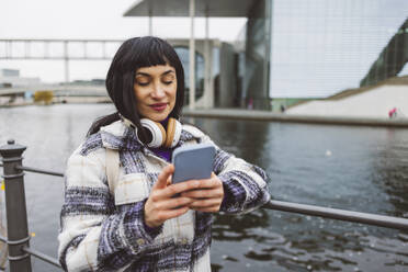 Frau, die am Fluss eine Textnachricht auf ihrem Smartphone schreibt - JCCMF11038