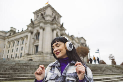 Lächelnde Frau genießt das Hören von Musik über drahtlose Kopfhörer - JCCMF11041