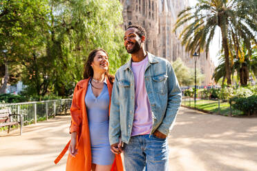 Multiracial beautiful happy couple of lovers dating at Sagrada Familia, Barcelona - Multiethnic tourists travelling in Europe and visiting a city in Spain, concepts about tourism and people lifestyle - DMDF08172