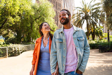 Multiracial beautiful happy couple of lovers dating at Sagrada Familia, Barcelona - Multiethnic tourists travelling in Europe and visiting a city in Spain, concepts about tourism and people lifestyle - DMDF08173