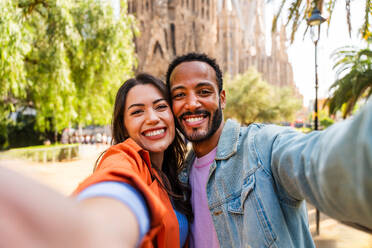 Multiracial beautiful happy couple of lovers dating at Sagrada Familia, Barcelona - Multiethnic tourists travelling in Europe and visiting a city in Spain, concepts about tourism and people lifestyle - DMDF08176