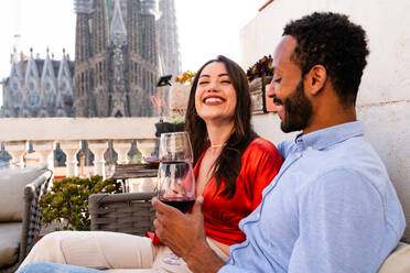 Multiracial beautiful happy couple of lovers dating on rooftop balcony at Sagrada Familia, Barcelona - Multiethnic people having romantic aperitif on a terrace with city view , concepts about tourism and people lifestyle - DMDF08192